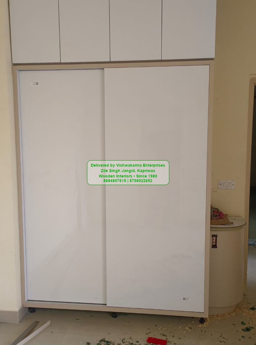 White sliding-door wardrobe with overhead loft cabinets in a finished apartment bedroom
